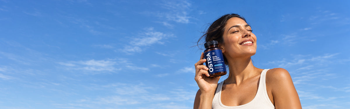 Woman outdoors under a bright blue sky holding OSTRA Daily Screen Support